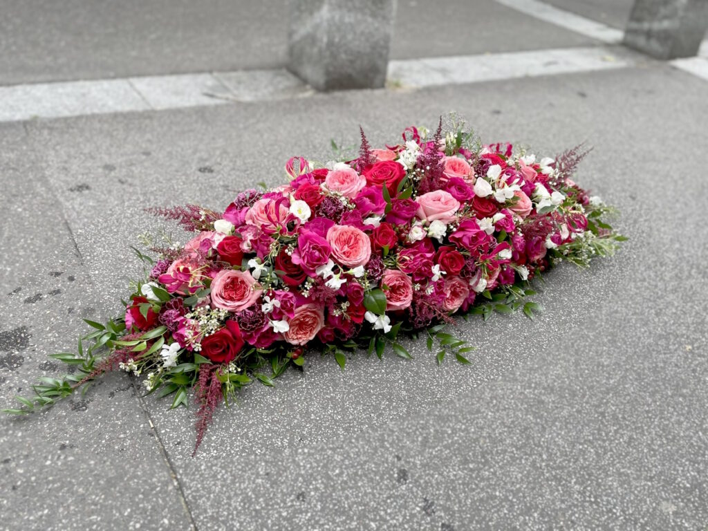 Dessus de cercueil de forme classique, composées de roses et fleurs plus champêtres, dans des tons roses, rouges, fuchsias