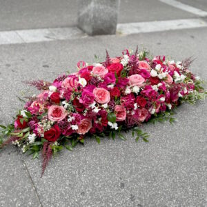 Dessus de cercueil de forme classique, composées de roses et fleurs plus champêtres, dans des tons roses, rouges, fuchsias
